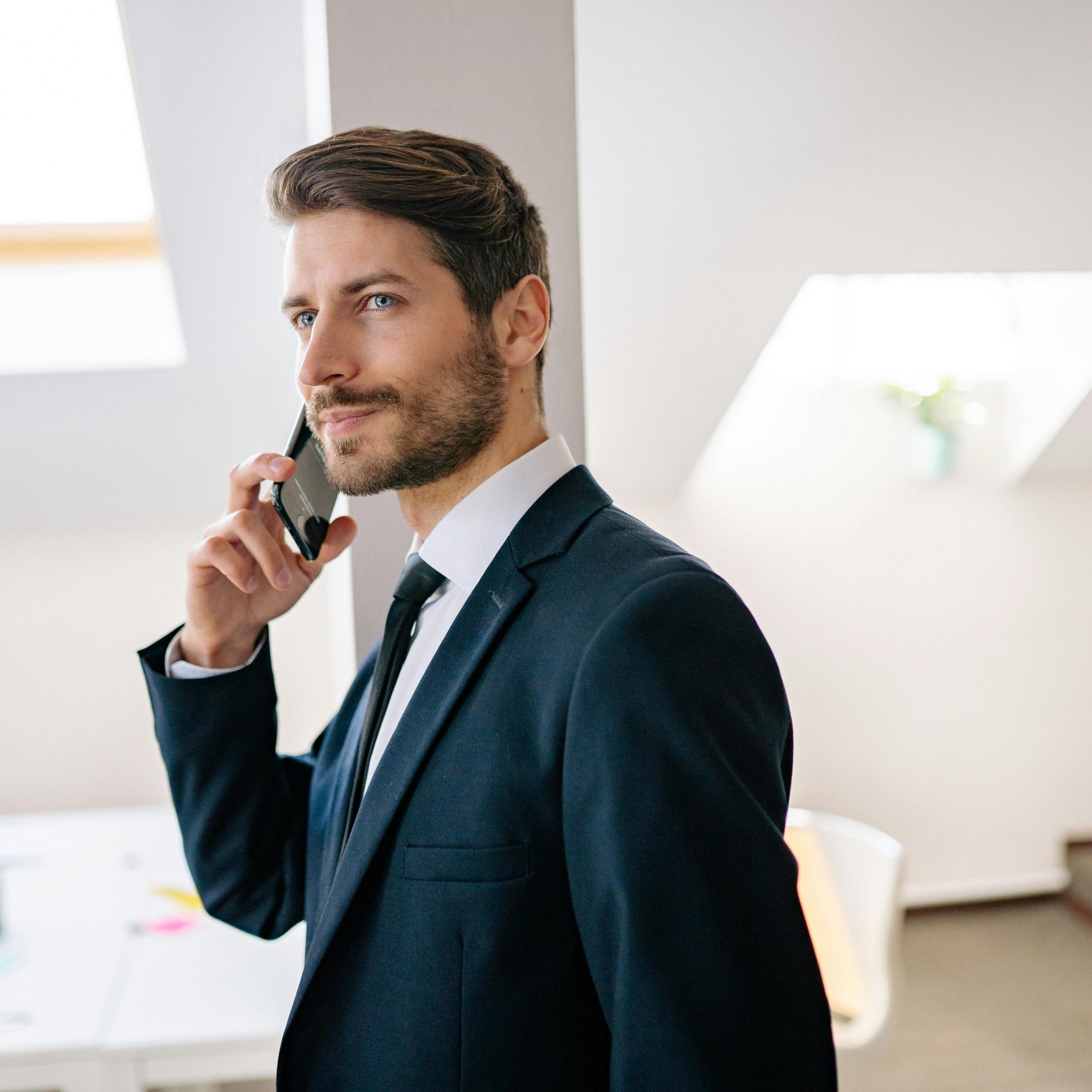 Professional businessman in a suit making a phone call in a modern office setting.